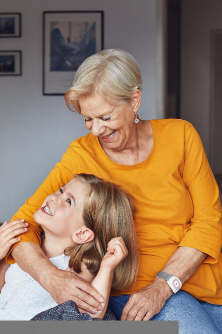 Eine Großmutter mit ihrer Enkelin. Die Oma trägt einen Hausnotruf-Sender am Handgelenk.