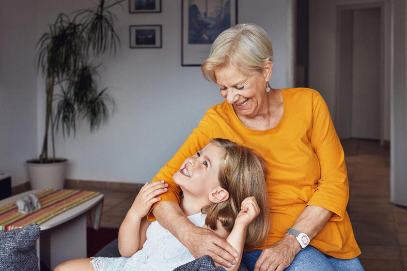 Eine Großmutter mit ihrer Enkelin. Die Oma trägt einen Hausnotruf-Sender am Handgelenk.