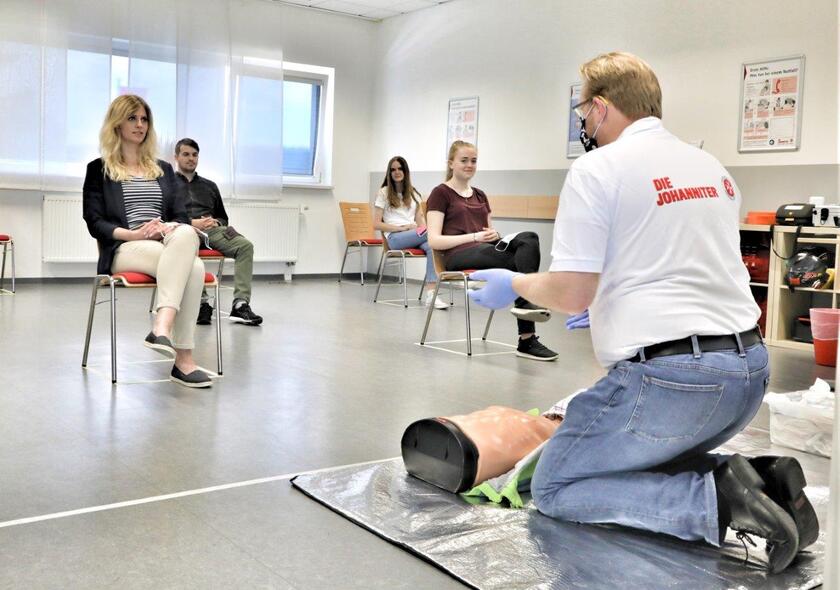 Erste-Hilfe-Trainer mit Alltagsmaske und Kursteilnehmer mit Sicherheitsabstand