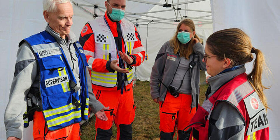 Vier Mitglieder des EMTs der Johanniter stehen vor einem Behandlungszelt. 