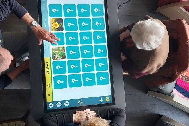 Senioren in der Tagespflege spielen Memorie an dem CareTable