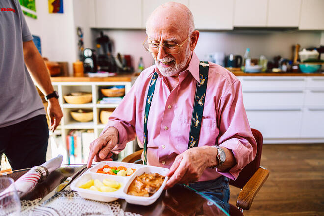 Hauslieferung eines Menüs: Senior genießt Mahlzeit am gedeckten Tisch
