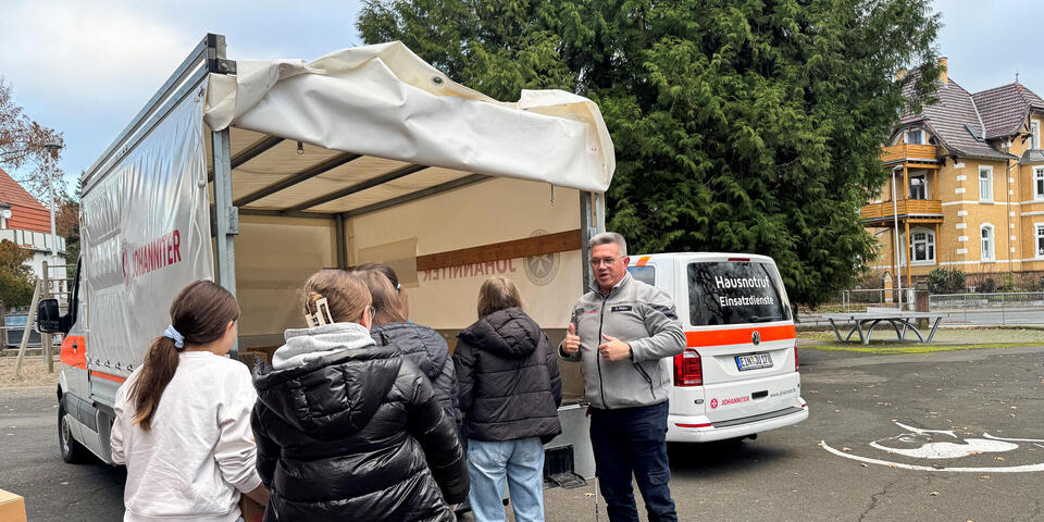 Kinder beladen einen LKW mit Paketen. Ein Mann in Johanniter-Kleidung steht daneben