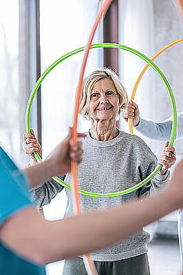 Physiotherapeutin mit zwei Seniorinnen, die Hula Hoop Reifen halten.