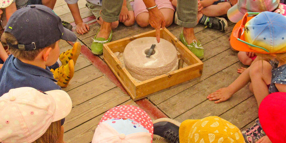 Kinder sitzen um eine Handgetreidemühle