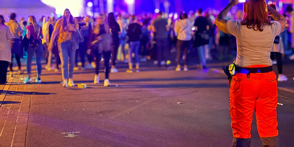 Eine Johanniterin schaut auf eine Menschenmenge. Es ist Nacht und im Hintergrund ist eine Bühne mit Lichteffekten