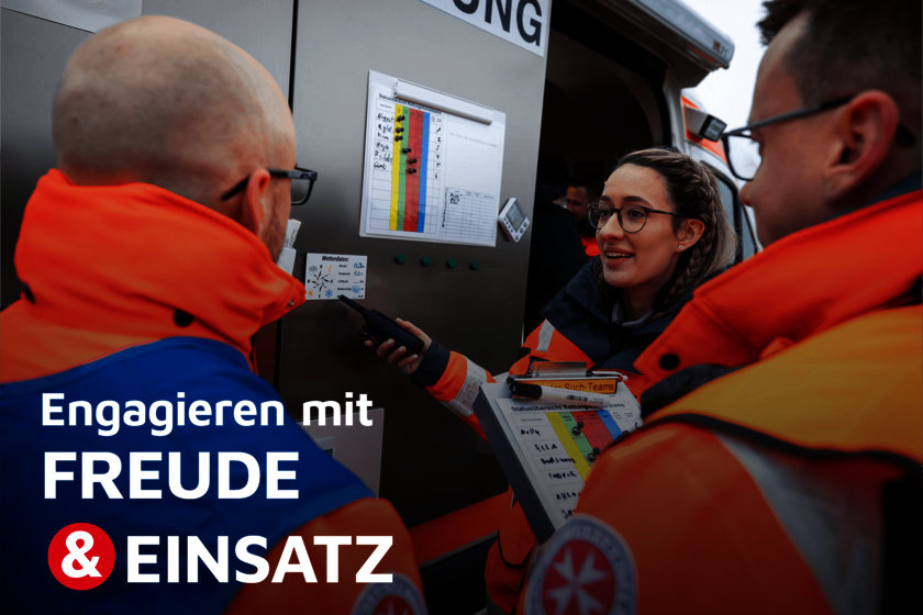 Drei Einsatzkräfte in heller Einsatzkleidung besprechen einen Einsatzplan an einem Rettungsfahrzeug, eine Frau mit geflochtenen Haaren spricht ins Funkgerät und hält ein Klemmbrett mit farbiger Statusübersicht.