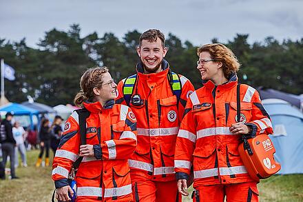 Drei Ehrenamtliche im Sanitätsdienst spazieren über ein Festivalgelände.