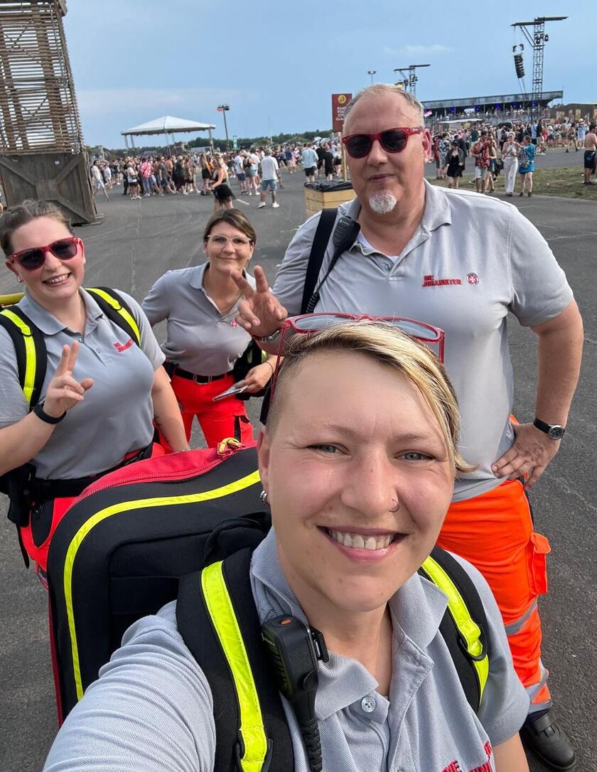 Vier ehrenamtliche Helfende der Johanniter laufen über ein Festival-Gelände. Sie tragen Einsatzkleidung in Grau und Orange sowie Einsatzrucksäcke.