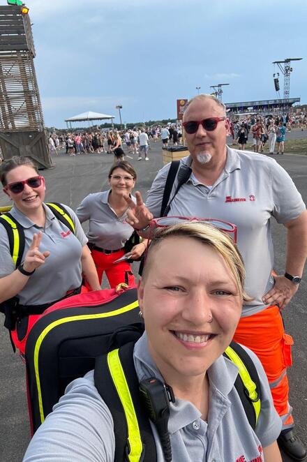 Vier ehrenamtliche Helfende der Johanniter laufen über ein Festival-Gelände. Sie tragen Einsatzkleidung in Grau und Orange sowie Einsatzrucksäcke.