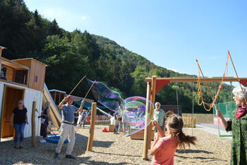 Ein Mann macht große Seifenblasen im Waldkindergarten
