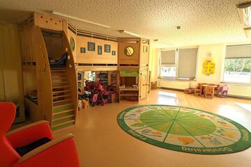 Blick in den Spielraum mit einem großen runden Teppich und einer Spielfläche, die sich über zwei Ebenen erstreckt.