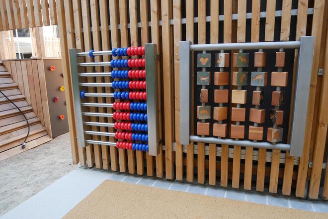 An einer Wand aus Holz Paneelen sind Kinderspiele angebracht.