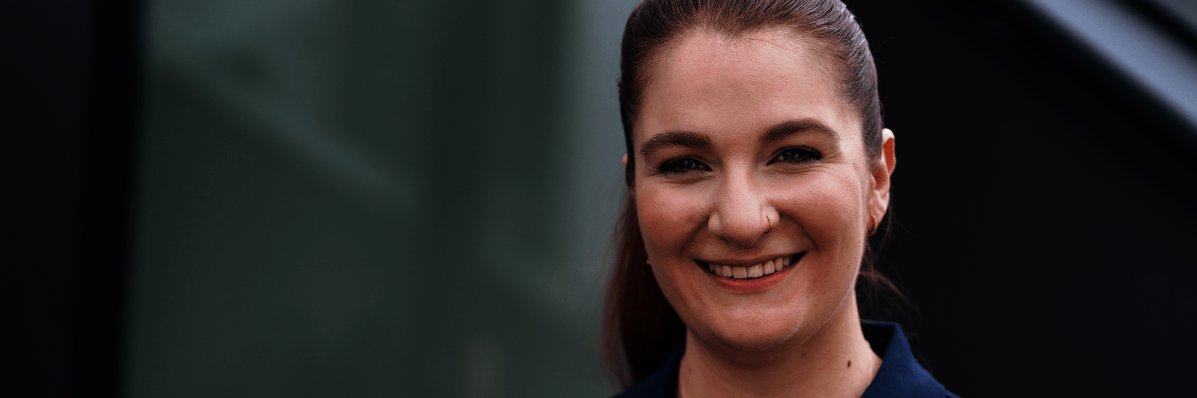 Junge Frau in dunkelblauem Polohemd und mit zurückgebundenen Haaren lächelt 