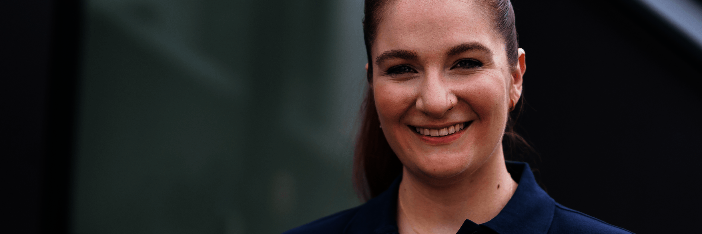 Junge Frau in dunkelblauem Polohemd und mit zurückgebundenen Haaren lächelt 