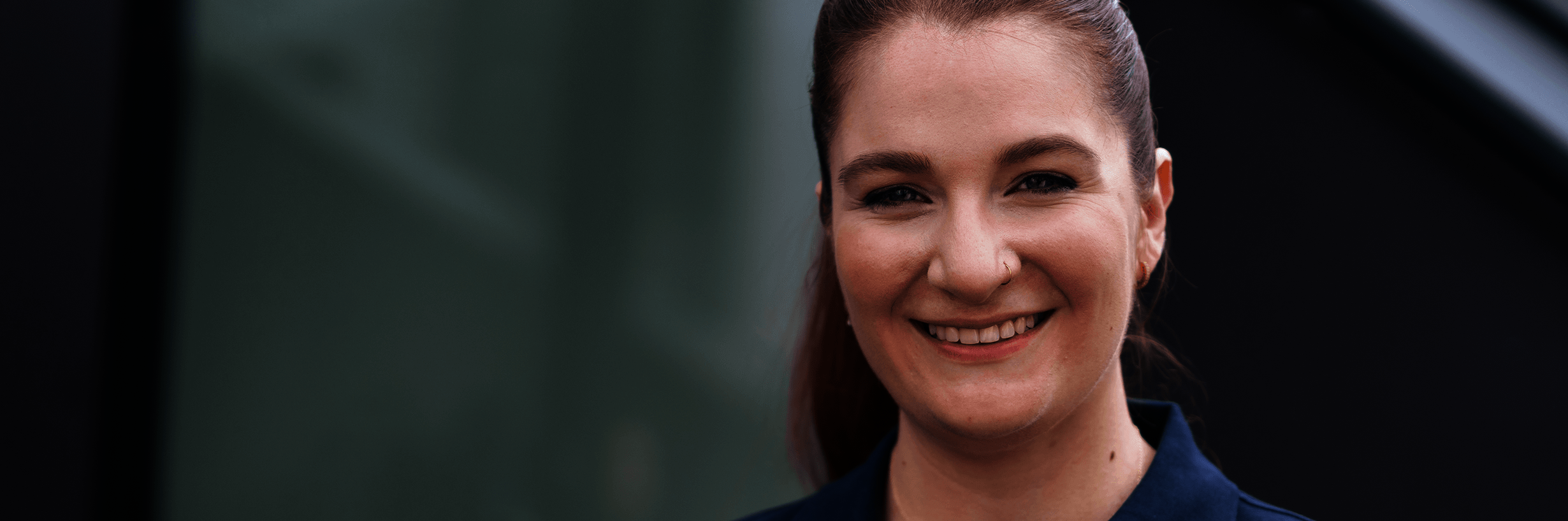 Junge Frau in dunkelblauem Polohemd und mit zurückgebundenen Haaren lächelt 