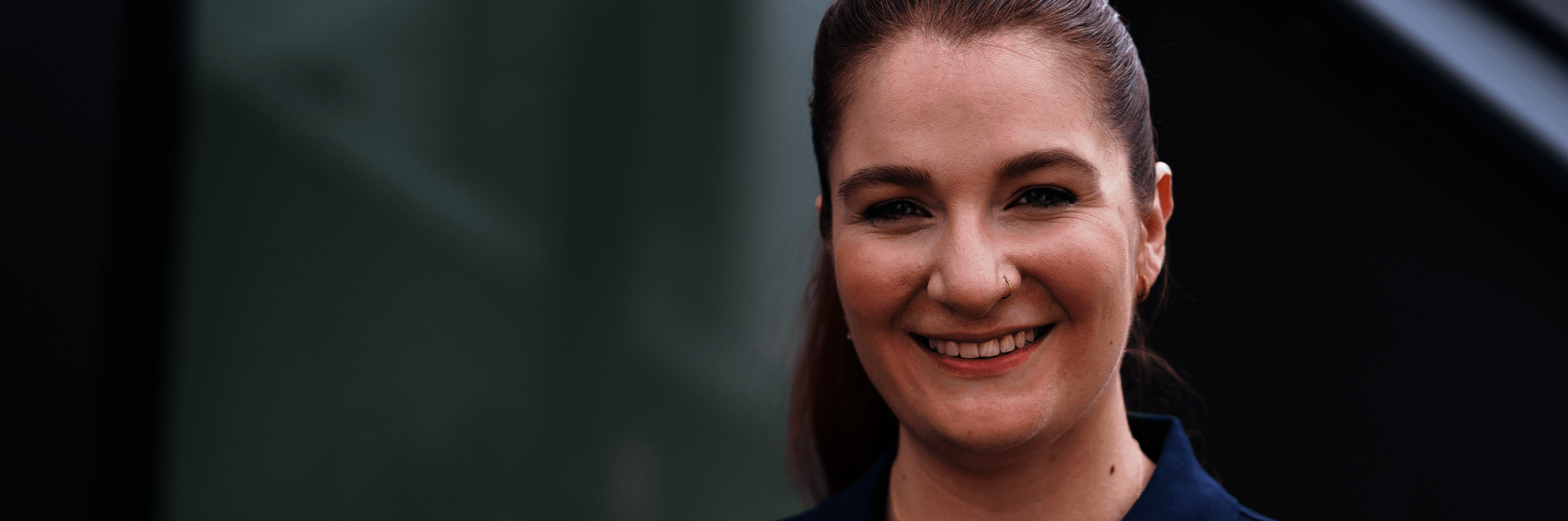 Junge Frau in dunkelblauem Polohemd und mit zurückgebundenen Haaren lächelt 