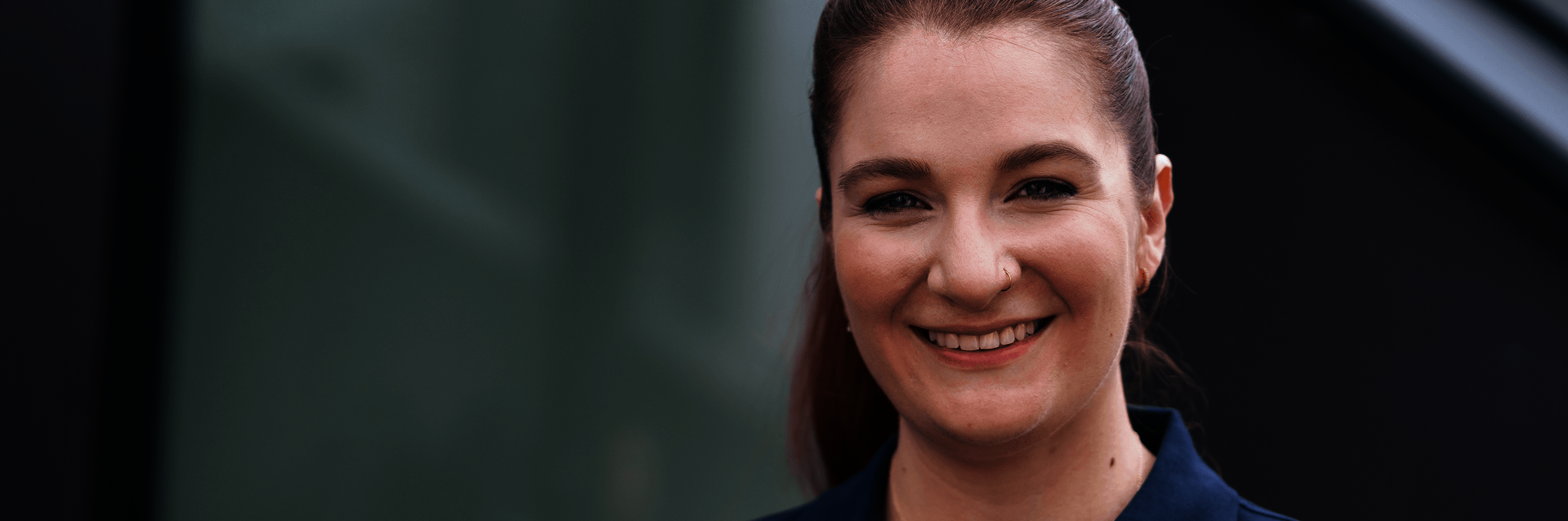 Junge Frau in dunkelblauem Polohemd und mit zurückgebundenen Haaren lächelt 