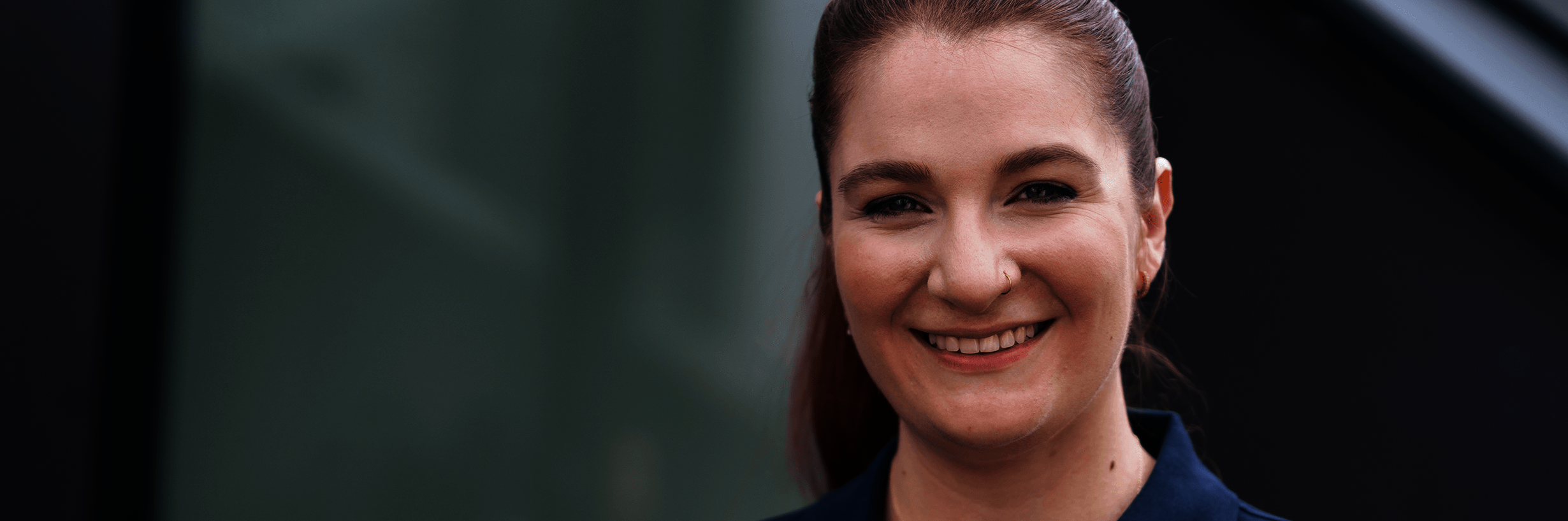 Junge Frau in dunkelblauem Polohemd und mit zurückgebundenen Haaren lächelt 