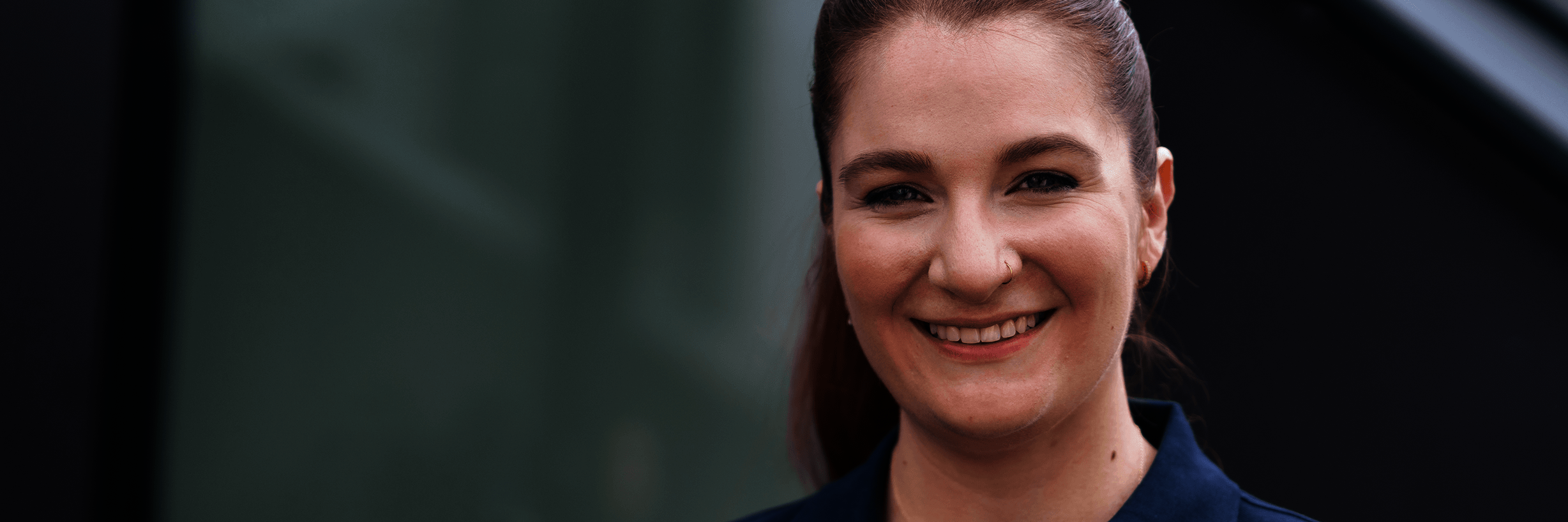 Junge Frau in dunkelblauem Polohemd und mit zurückgebundenen Haaren lächelt 