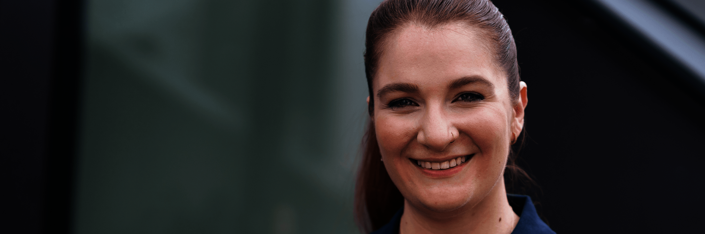 Junge Frau in dunkelblauem Polohemd und mit zurückgebundenen Haaren lächelt 