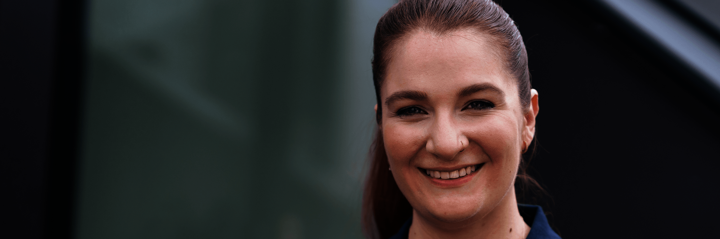 Junge Frau in dunkelblauem Polohemd und mit zurückgebundenen Haaren lächelt 