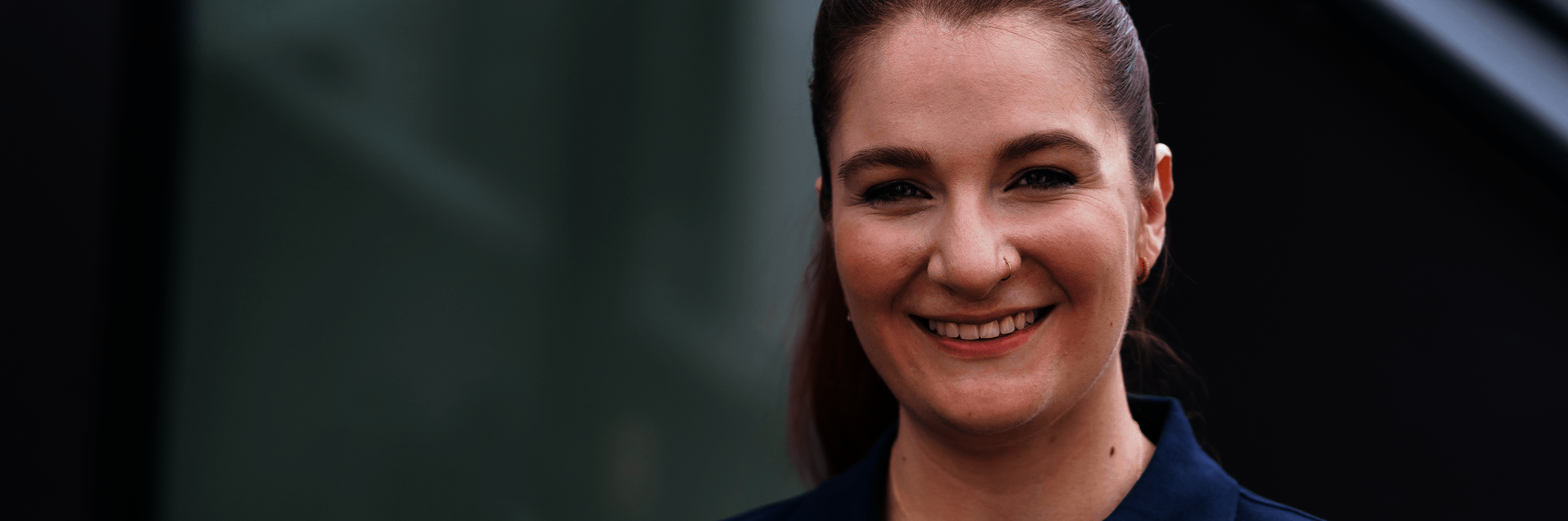 Junge Frau in dunkelblauem Polohemd und mit zurückgebundenen Haaren lächelt 