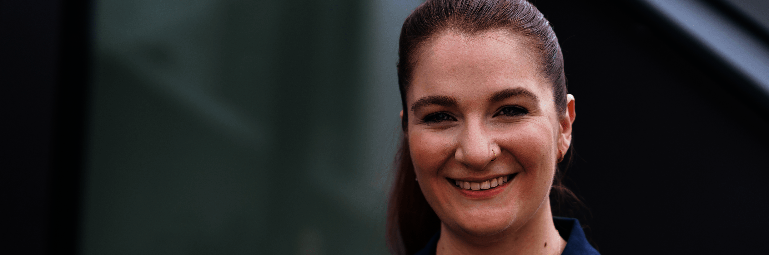 Junge Frau in dunkelblauem Polohemd und mit zurückgebundenen Haaren lächelt 