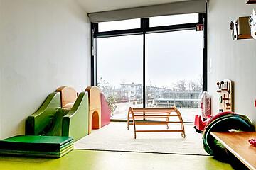 Heller Spielraum mit Rutsche, Kletterbogen und großen Fenstern.