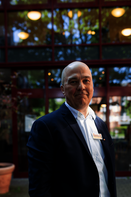 Ein Mann im Anzug steht vor einer Glasfassade mit Namensschild am Revers