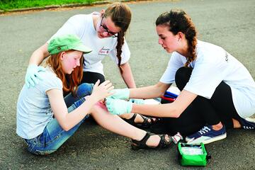 Zwei Schulsanitäterinnen versorgen ein Mädchen, das hingefallen ist.