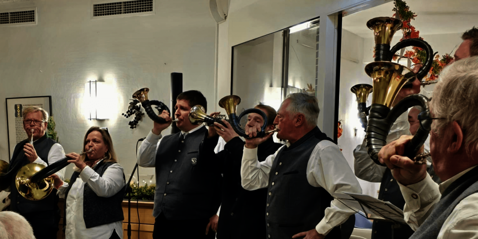 eine Gruppe Jagdhornbläser in weißen Hemden und grauen Westen spielt auf unterschiedlich großen Hörnern