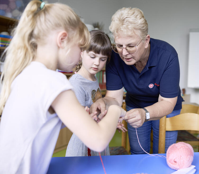 Eine Betreuerin hilft Kindern bei der Vorbereitung von Handarbeiten mit Wollknäulen.