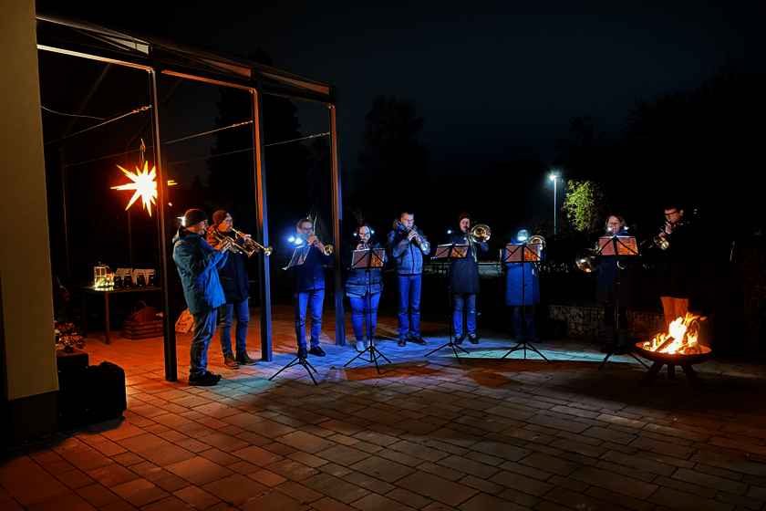 Posaunenchor auf einer Terrasse, die von einem leuchtenden Herrrnhuterstern und einer Feuerschale erleuchtet wird.