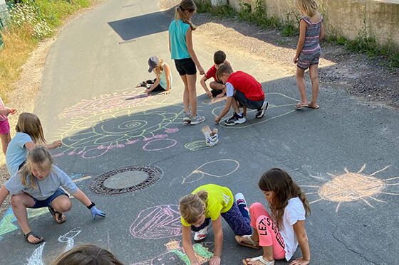 Kinder malen mit Kreide aus einen asphaltierten Weg 2