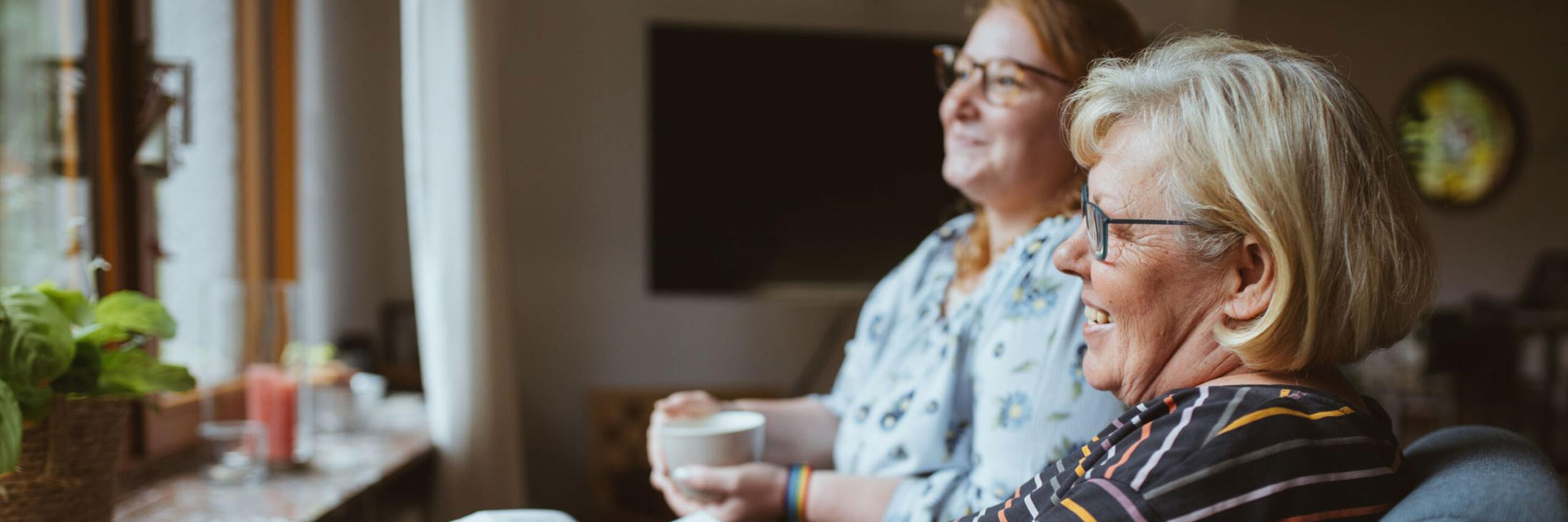 Eine Johanniter-Pflegefachkraft trinkt mit einer Kunden einen Kaffee mit Blick in den Garten in Wiesbaden.