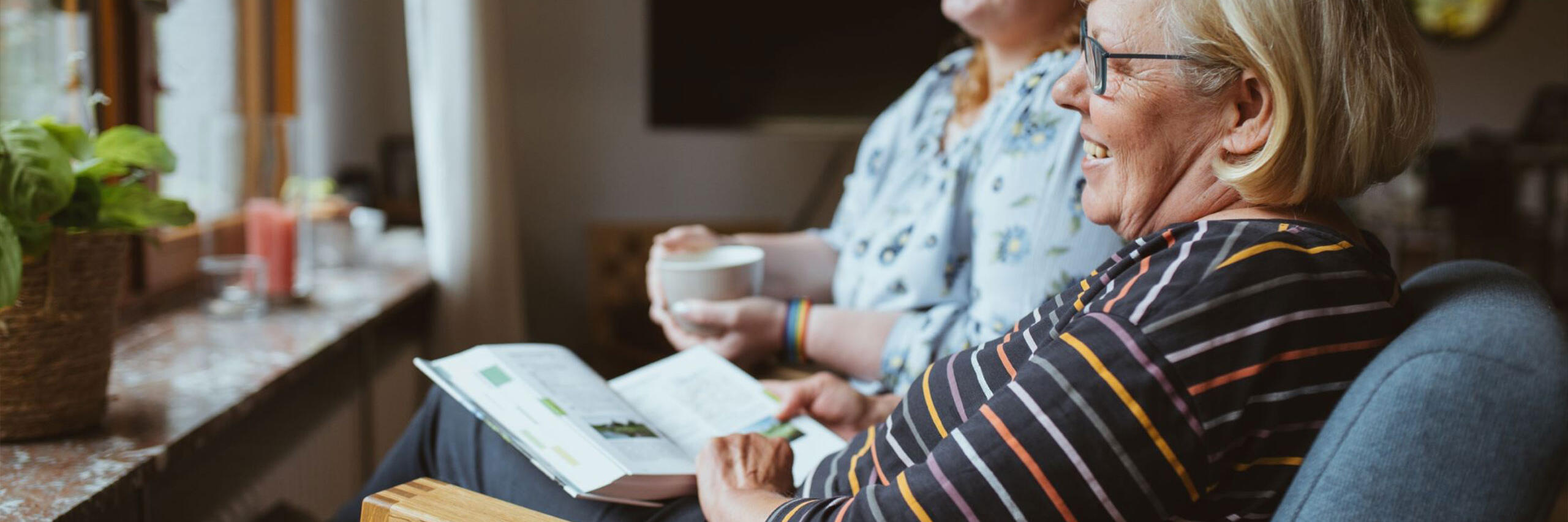 Eine Johanniter-Pflegefachkraft trinkt mit einer Kunden einen Kaffee mit Blick in den Garten in Wiesbaden.