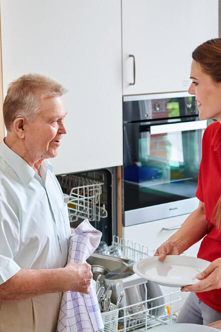 Eine Pflegerin der Johanniter räumt mit einem älteren Mann eine Spülmaschine aus.