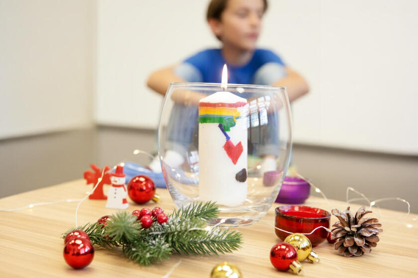 Unscharfer Junge im Hintergrund, vorn Weihnachtsdeko und leuchtende Kerze.