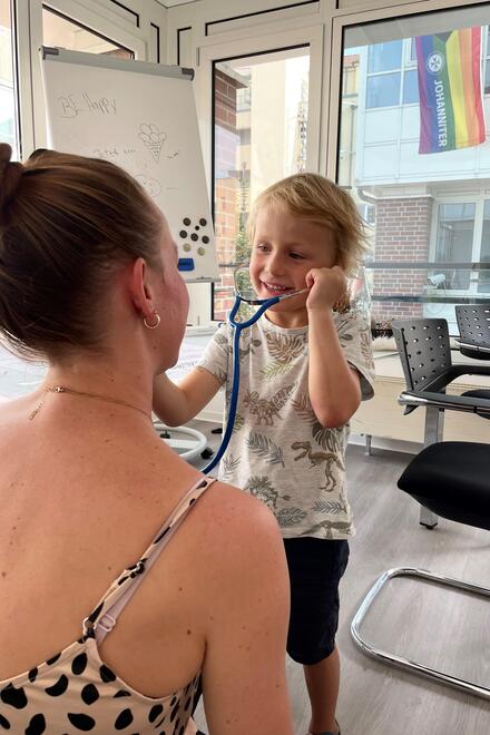 Ein junges Kind hört bei einer Frau den Herzschlag mit einem Stethoskop ab.