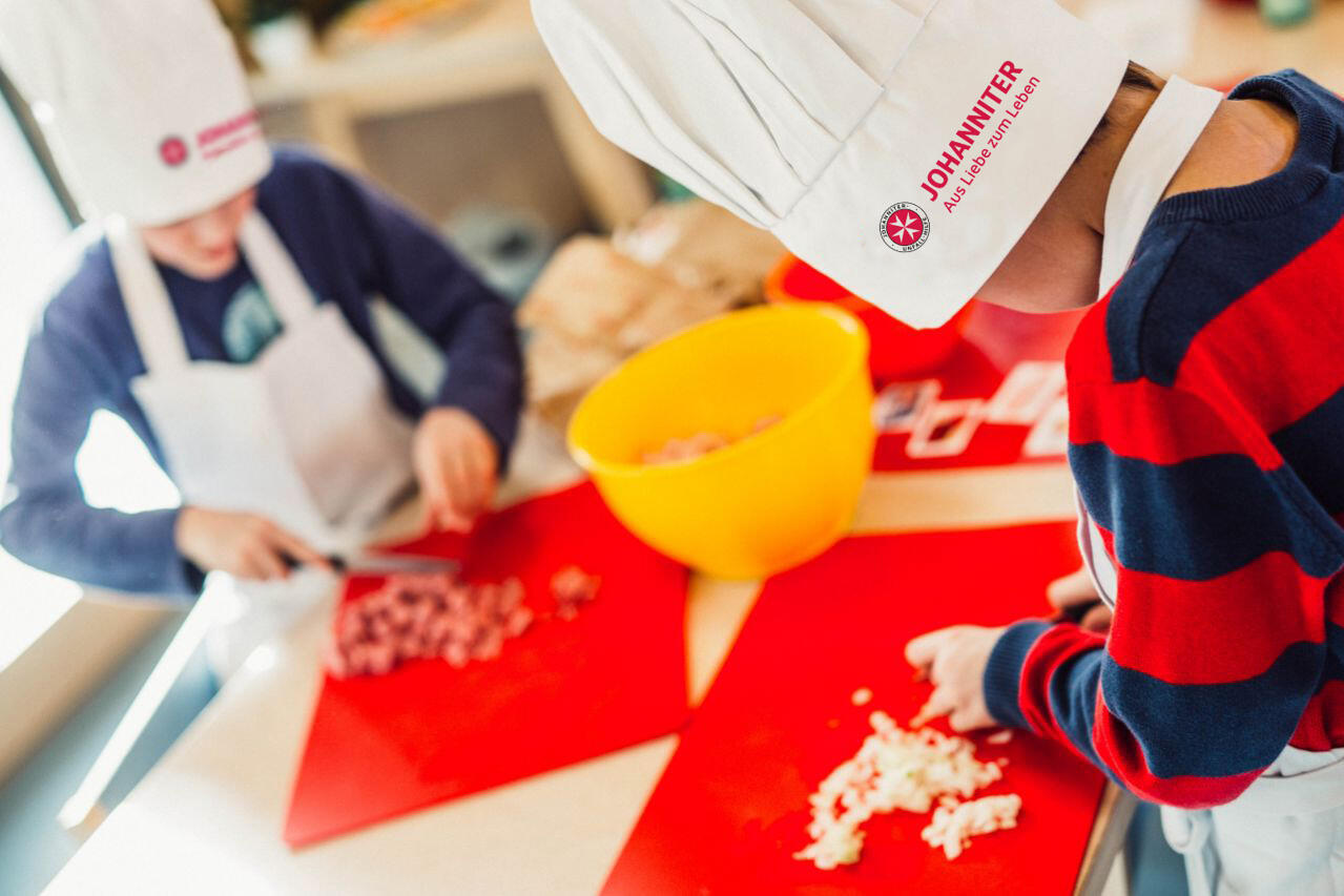 Kinder mit Kochmützen schneiden Zutaten.