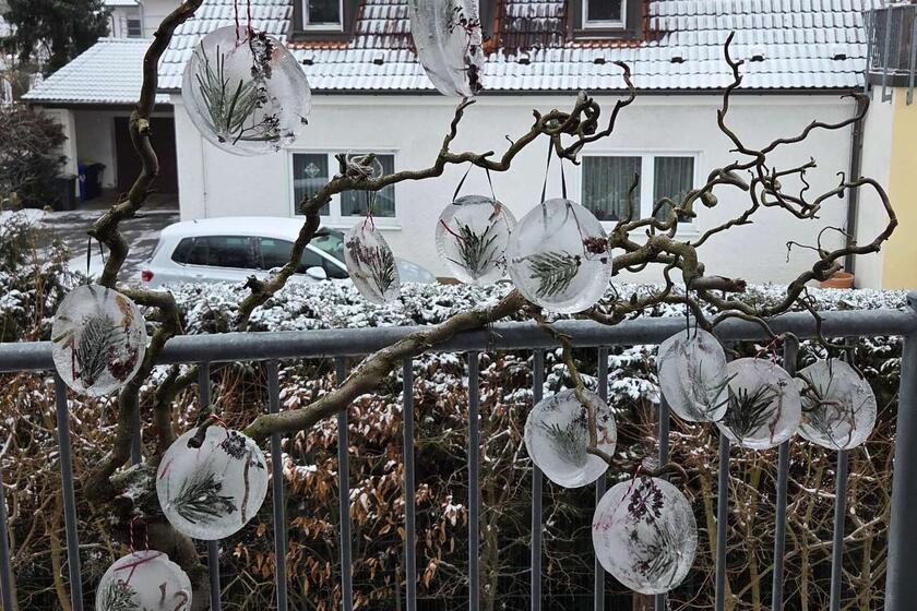 Gestaltete, eingefrorene Eiskugeln hängen an einem Strauch. Es ist winterlich und überall liegt Schnee.