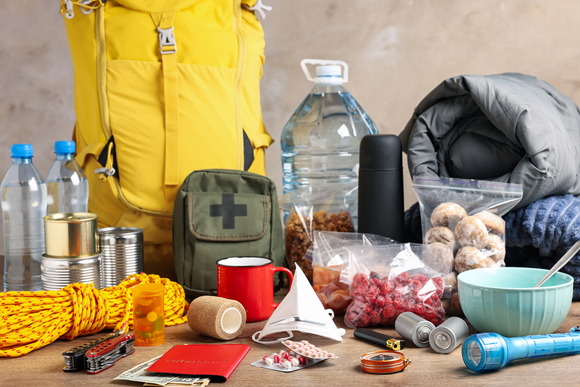 Notfallrucksack und Vorräte: Wasserflaschen, Konserven, Decke, Erste‑Hilfe‑Set, Taschenlampe, Lebensmittel und Medikamente.
