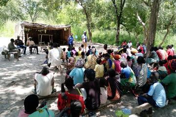 Eine Menschenmenge sitzt auf dem Boden. Vor ihnen steht ein Redner und eine Rednerin.