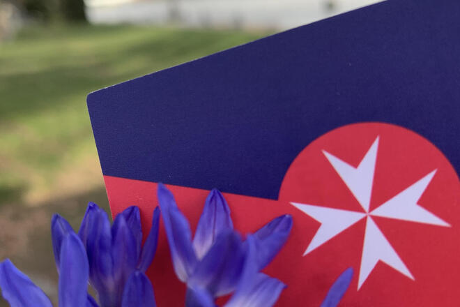 Lila Blumen mit einem Johanniter-Schild