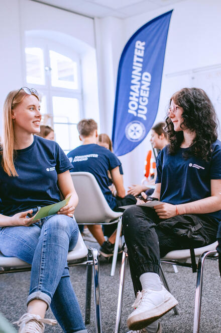 Zwei junge Frauen der Johanniter-Jugend unterhalten sich miteinander in einem Stuhlkreis.