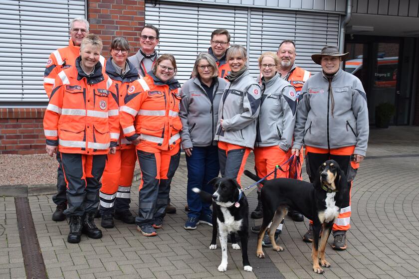 Teilnehmende an der Rettungshundeprüfung und zwei Hunde stehen in einer Gruppe vor dem Gebäude der Johanniter
