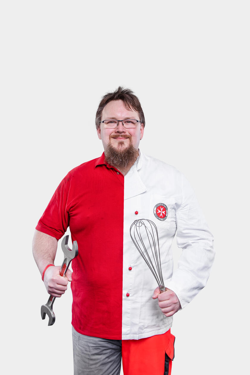 Ehrenamtlicher in Johanniterkleidung und Outfit welches er sonst in seinem Hauptjob in der Werkstatt trägt