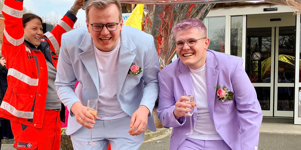 Ein Hochzeitspaar läuft geduckt unter hochgehaltenen Rettungsdecken durch