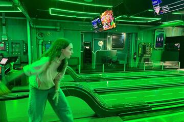 Ein Mädchen lässt die Bowlingkugel in die Bahn gleiten.